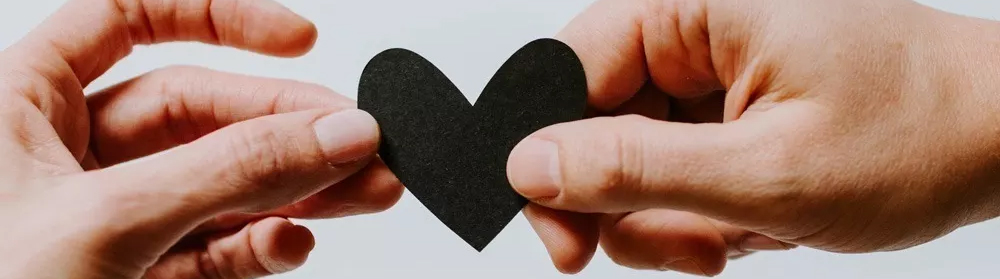 Zwei Hände die ein schwarzes Pappherz halten